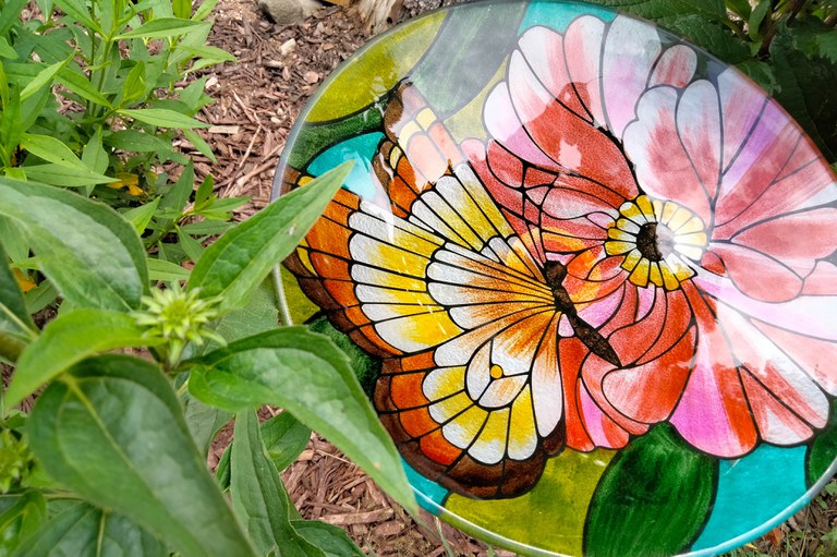 A glass birdbath serves as a water source in a pollinator friendly garden.
